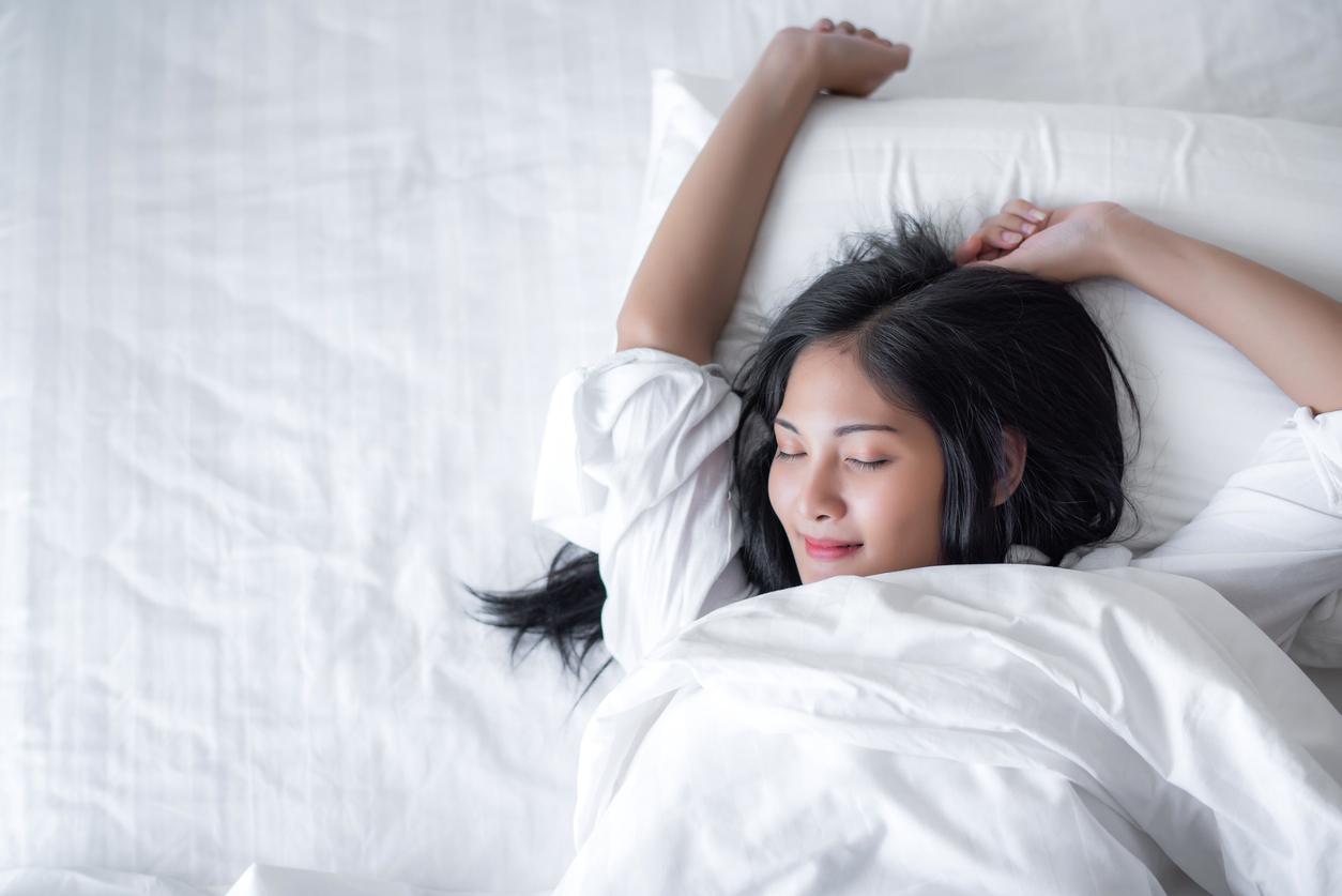 young woman wake up and make happy smile with white shirt at the white bed in the morning.